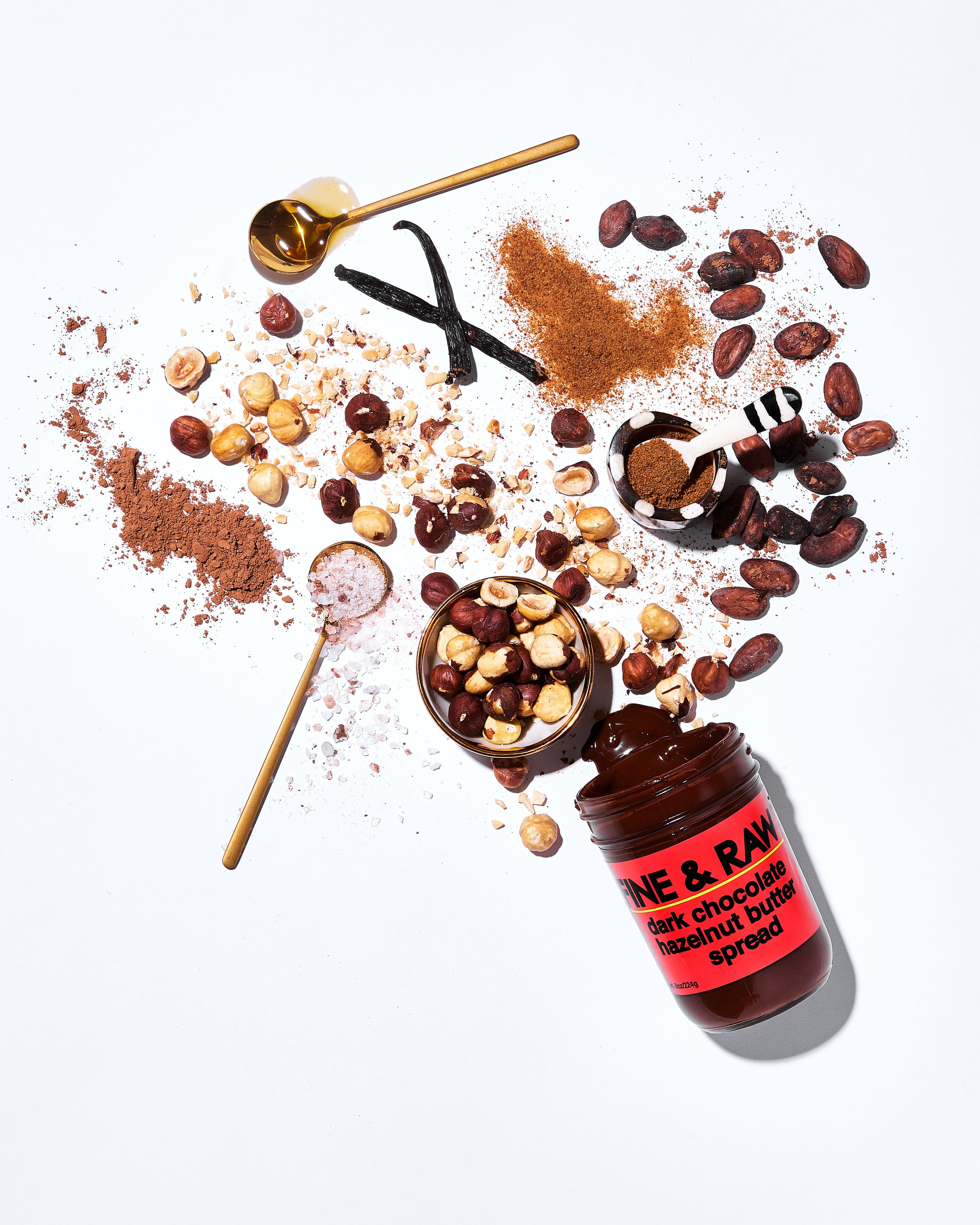 Open jar with individual ingredients (Organic hazelnuts, organic coconut sugar, organic cacao bean, organic cacao powder, organic whole ground vanilla, sea salt) displayed outside of the jar